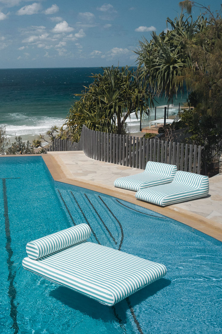 an empty swimming pool with two lounge chairs next to it and the ocean in the background