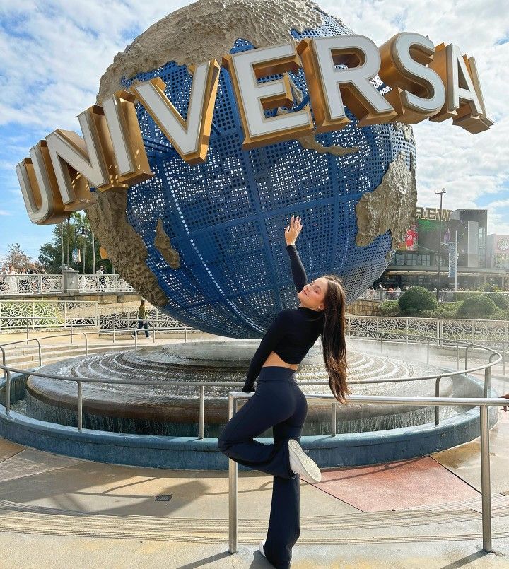 a woman standing in front of a giant sign that says universal with her arms up