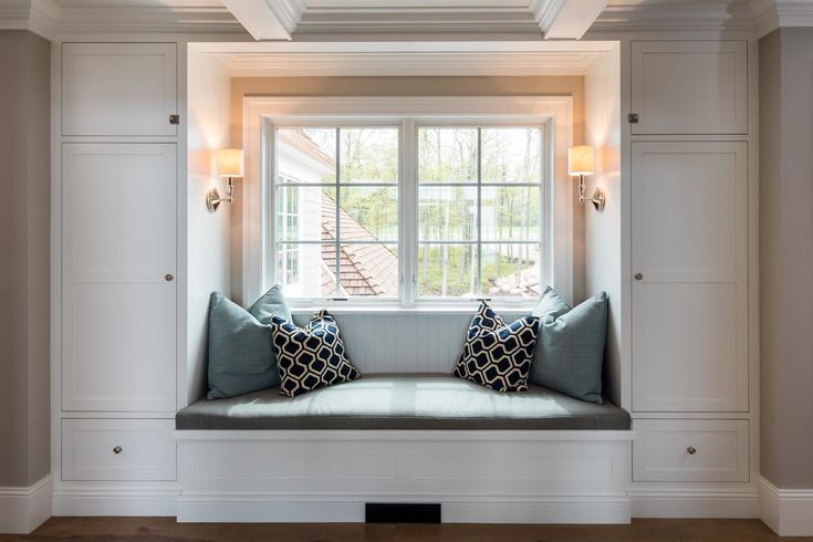 a window seat with two pillows on it in the middle of a room that has white paneling and built - in shelving