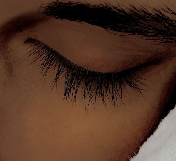 the eye of a person with long black hair and thick eyelashes on their face is covered by a white towel