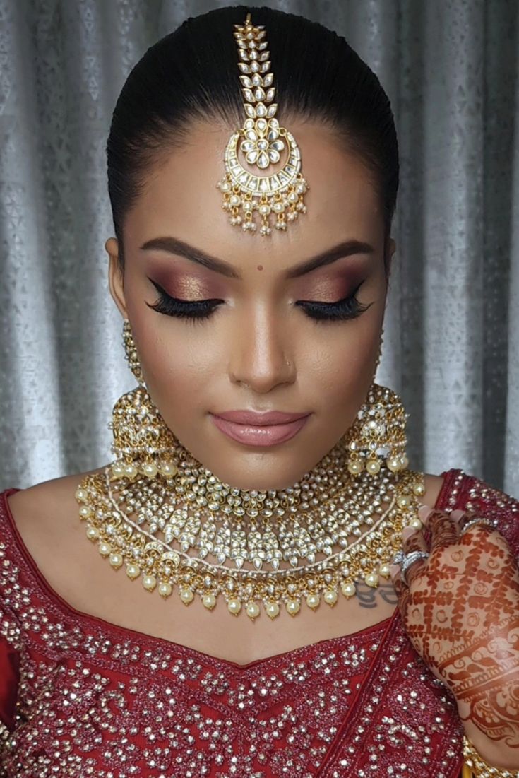 a woman wearing a red and gold bridal outfit with her hands on her chest