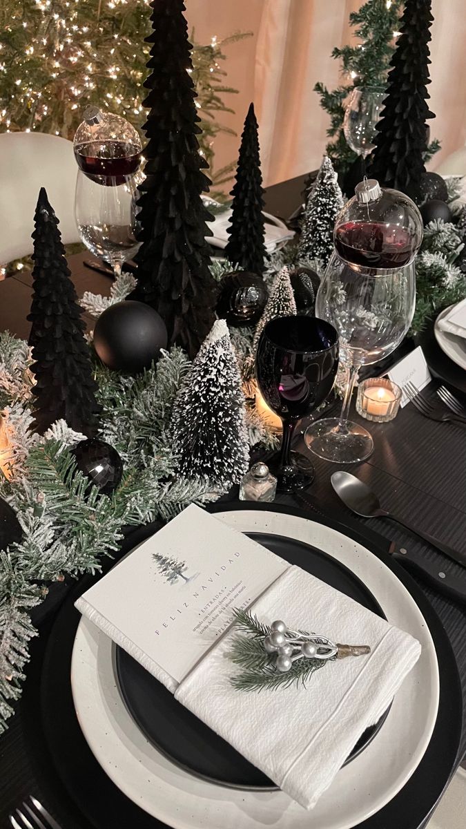 the table is set with black and white plates, napkins, silverware and christmas trees