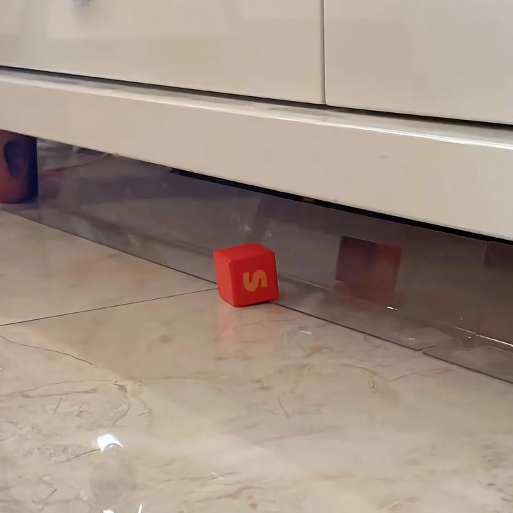 a red block sitting on the ground next to a white cabinet