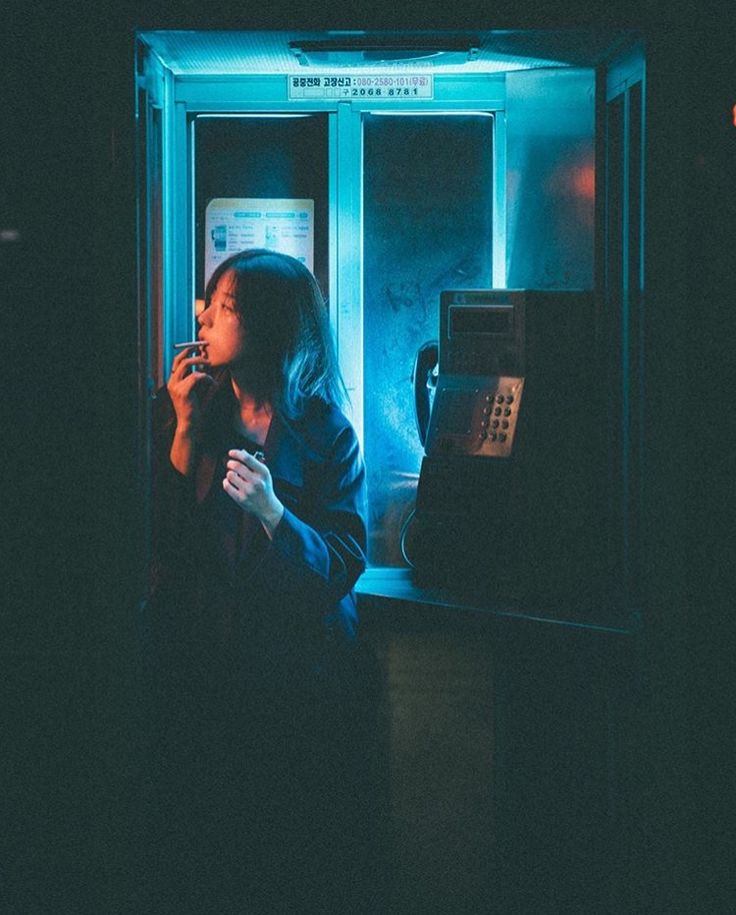 a woman standing in front of a phone booth with her hand on her mouth and looking out the window