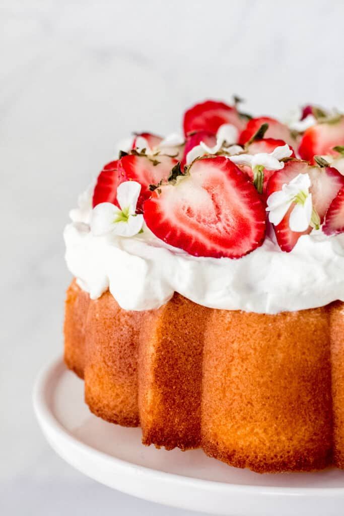 a cake with whipped cream and strawberries on top sits on a white platter