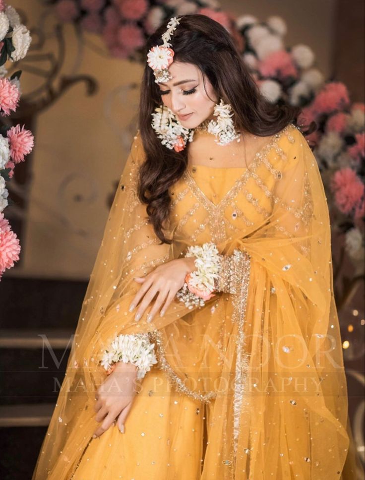 a woman in yellow dress with flowers on her head and veil over her face, posing for the camera