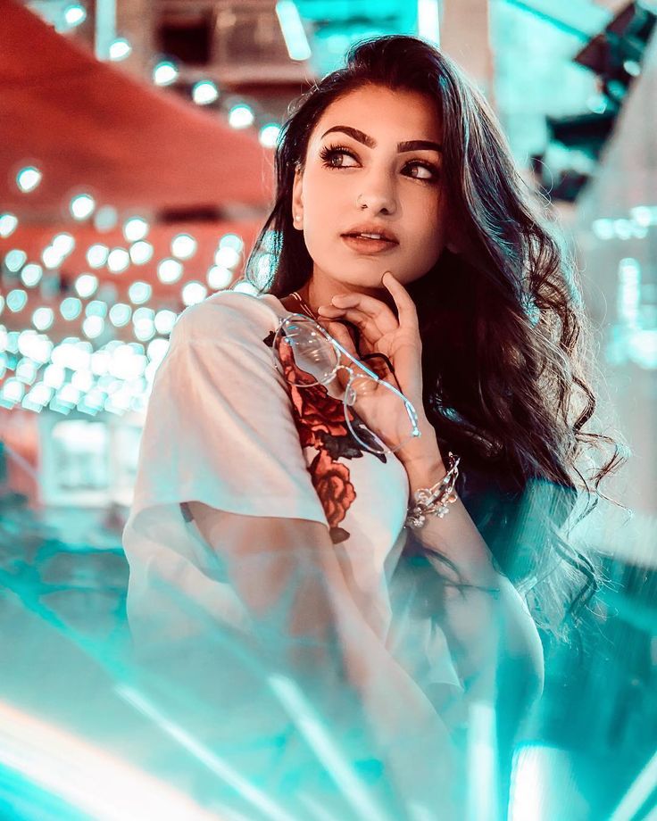 a woman with long hair posing for a photo in front of a neon light background