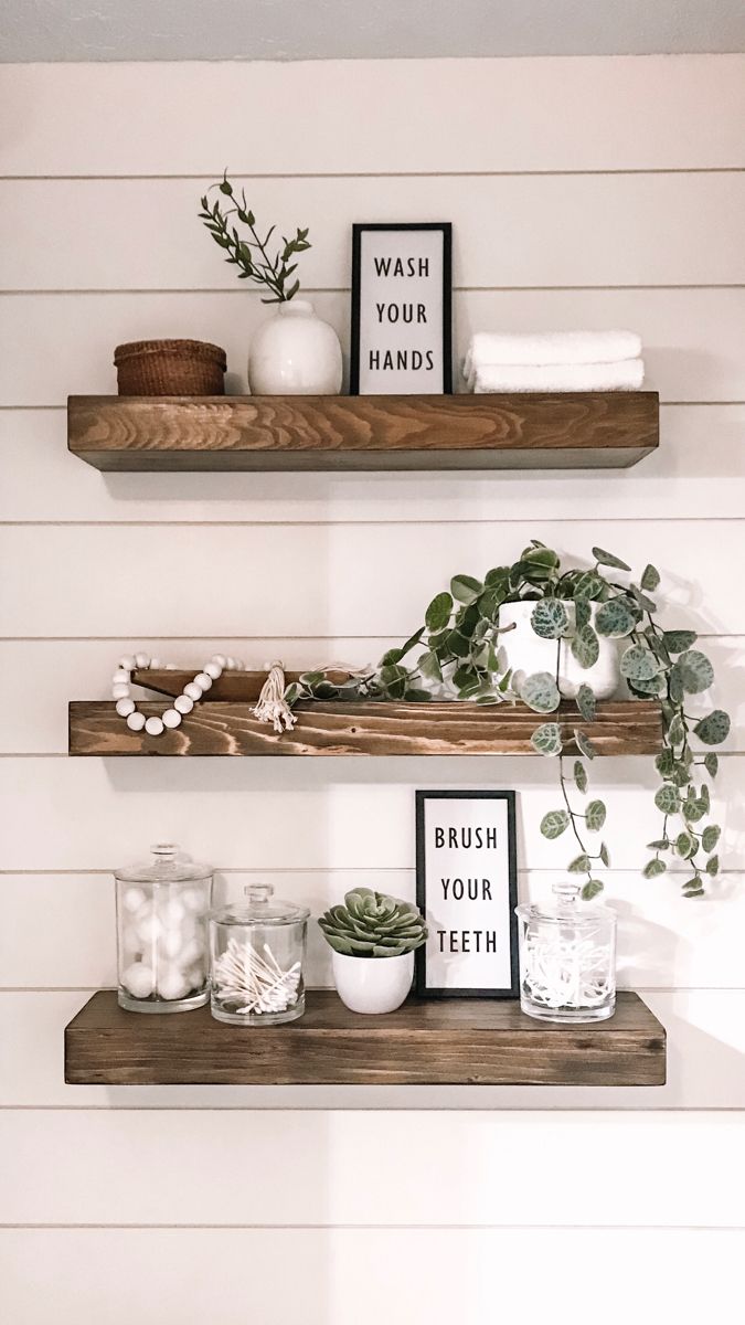 two wooden shelves with plants, candles and pictures on them in the corner of a bathroom