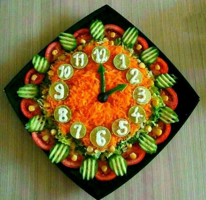 a clock made out of vegetables and other food items on a black plate with white numbers