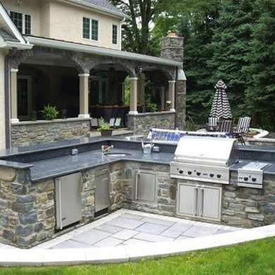 an outdoor kitchen is built into the side of a house with stone counters and grills