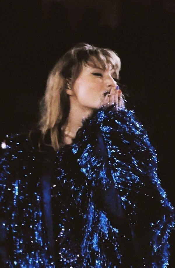 a woman in blue sequins is holding her hand up to her face while she sings