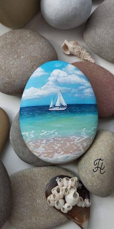 a rock with a sailboat painted on it sitting next to some rocks and seashells