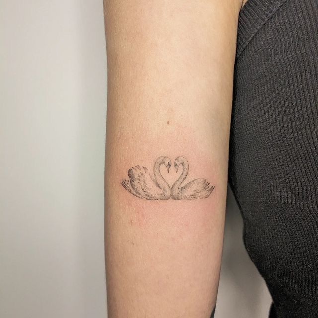 a woman's arm with two swans in the shape of a heart on it