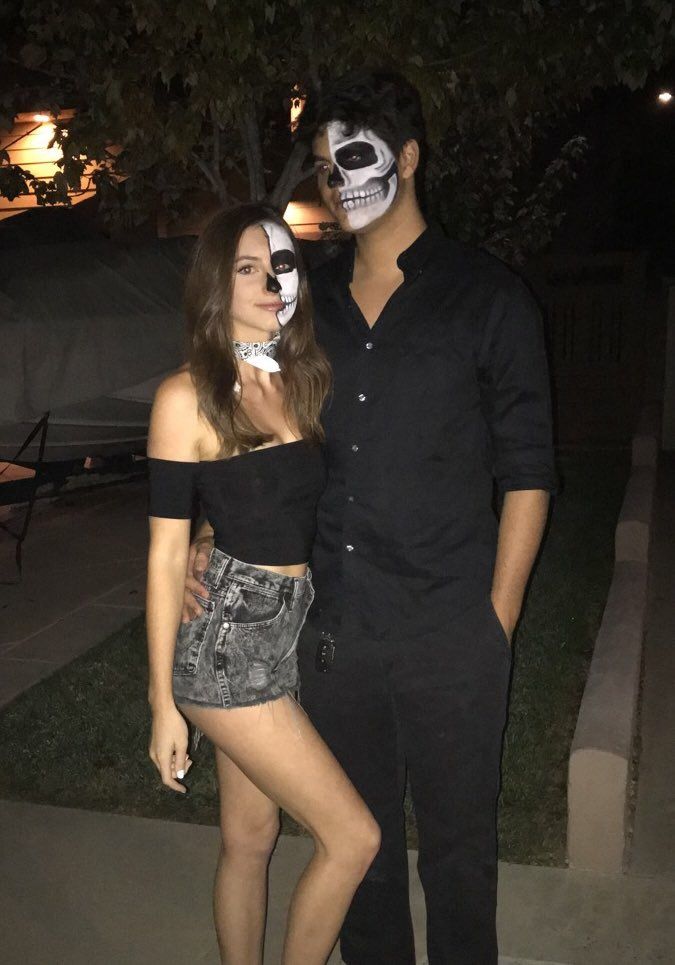 a man standing next to a woman in a skeleton makeup on her face at night