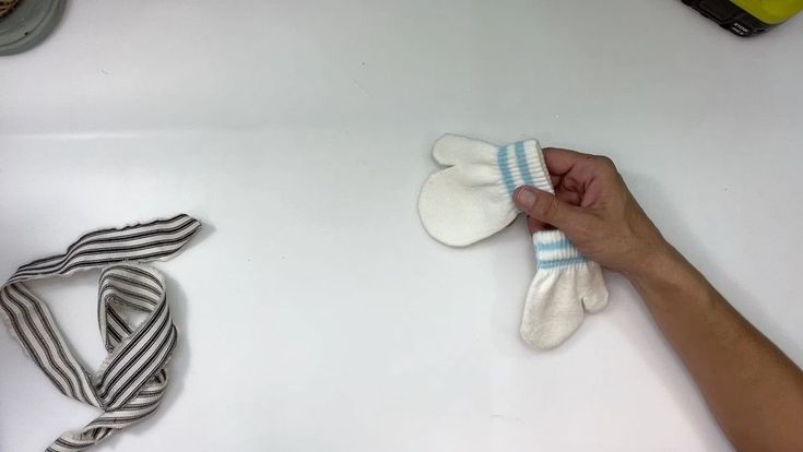 someone is holding two mittens on top of a white surface next to other items