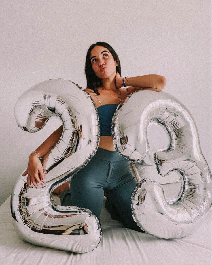 a woman sitting on top of a bed holding two large silver balloons in the shape of numbers