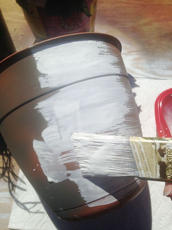 a person is holding a paintbrush and painting a pot with white paint on it