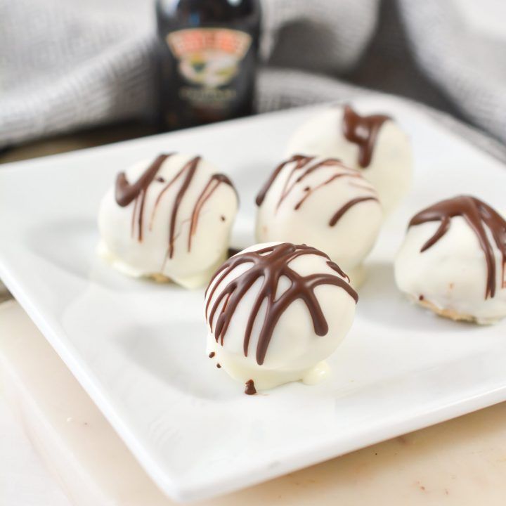 four chocolate covered desserts on a white plate with a bottle of beer in the background