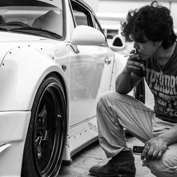 a man sitting on the ground next to a white sports car with his hand in his mouth