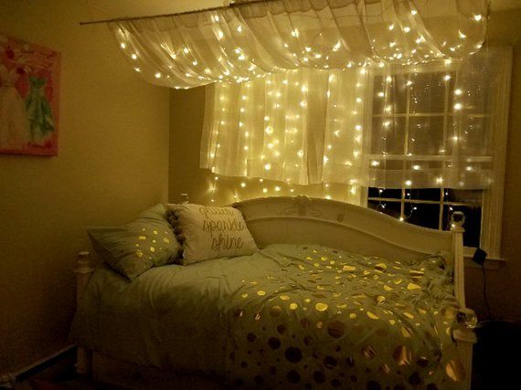 a bed sitting under a window covered in lights