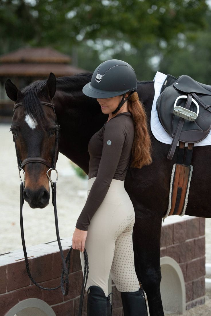 a woman in riding gear standing next to a horse