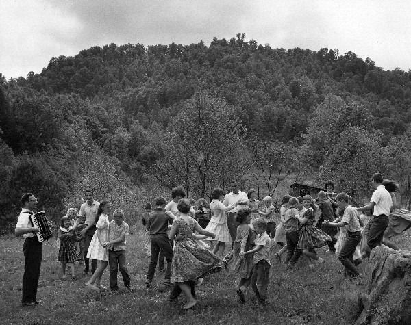 an old black and white photo of people playing in the grass with trees in the background