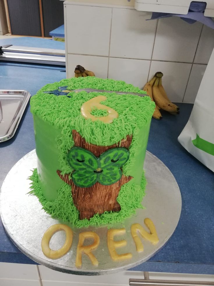 a green cake with an owl on it sitting on top of a counter next to bananas