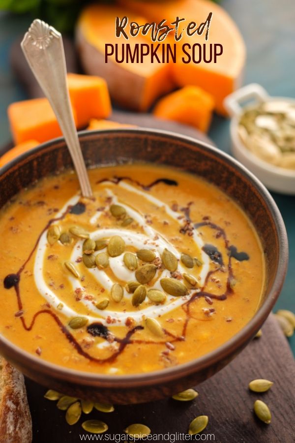 a bowl of pumpkin soup with whipped cream and pumpkin seeds on the side, next to sliced carrots