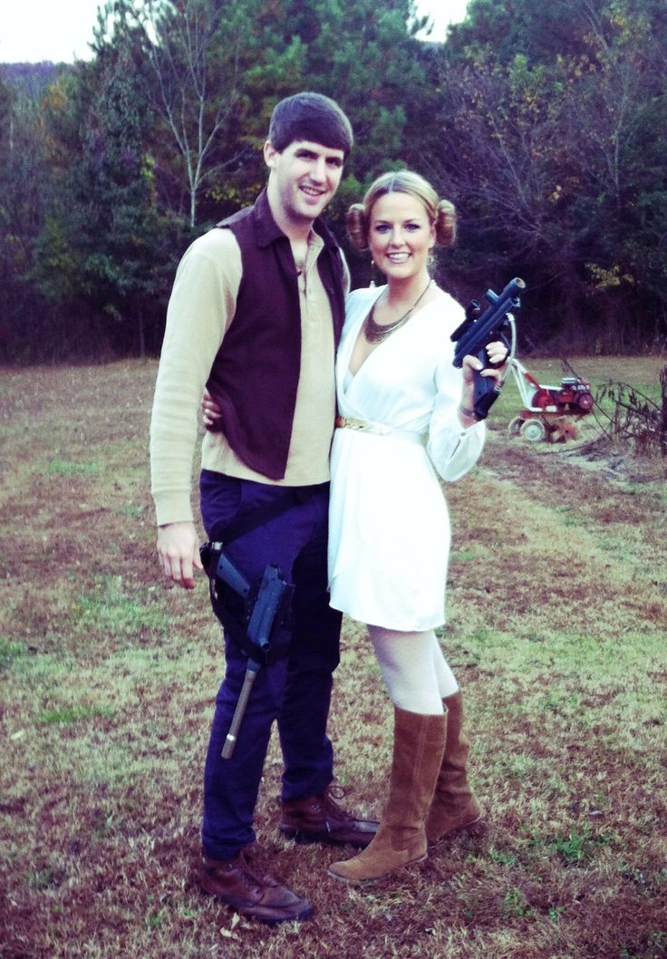 a man and woman standing next to each other in a field with trees behind them