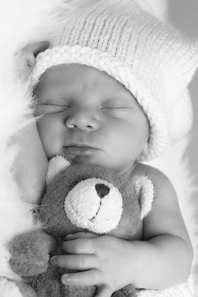 a baby sleeping with a teddy bear in it's arms and wearing a knitted hat