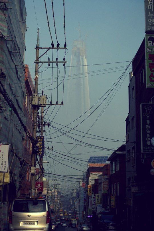 cars are parked on the street in front of tall buildings and power lines above them