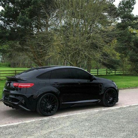 a black car is parked on the side of the road in front of some trees