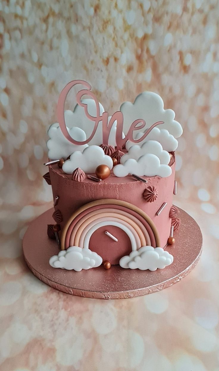 there is a pink cake with clouds and a rainbow on the top that says one