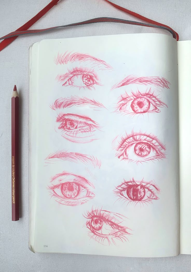 an open book with drawings of eyes and pencils on it next to a red pen