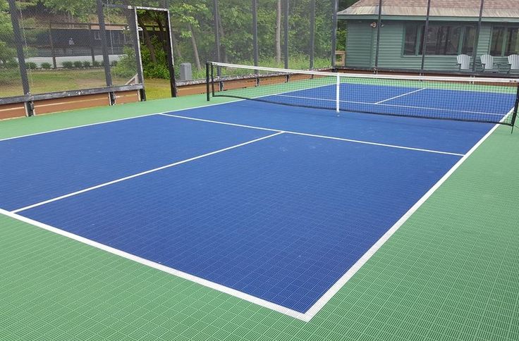 two blue tennis courts with trees in the backgroud and houses in the background