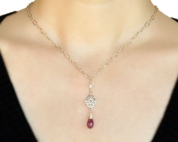 The ruby is probably the most well-known gemstone in the world, and its name will forever be linked with its striking red color. No other gemstone shares such a strong link with feelings of love and passion. Ruby is the birthstone for July and the gem for the 15th and 40th anniversaries. This necklace is in a classic style, incredibly elegant and refined. A ruby briolette stone dangles from a gold filigree; three tiny freshwater seed pearls are wire wrapped to the chain to add more dimension and Red Ruby Gemstone Necklaces, Red Ruby Gemstone Necklace, Elegant Ruby Briolette Necklace, Dainty Ruby Gemstone Birthstone Necklace, Red Ruby Necklace With Gemstone Accents, Red Ruby Birthstone Necklaces, Elegant Ruby Birthstone Necklace, Classic Red Birthstone Jewelry, Ruby Briolette Necklace In Fine Jewelry Style