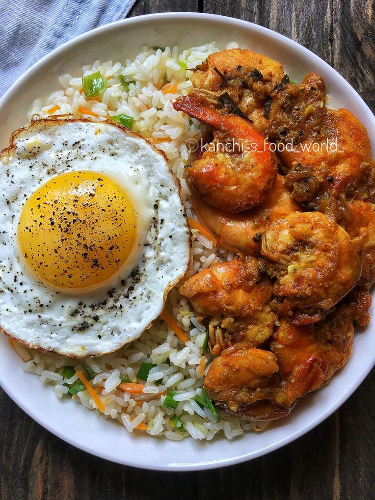 a white plate topped with rice and shrimp next to an egg on top of it