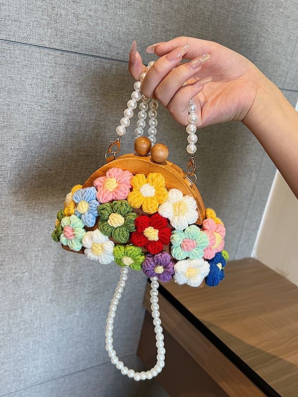 a hand holding a purse with flowers on it and pearls hanging from the handle,