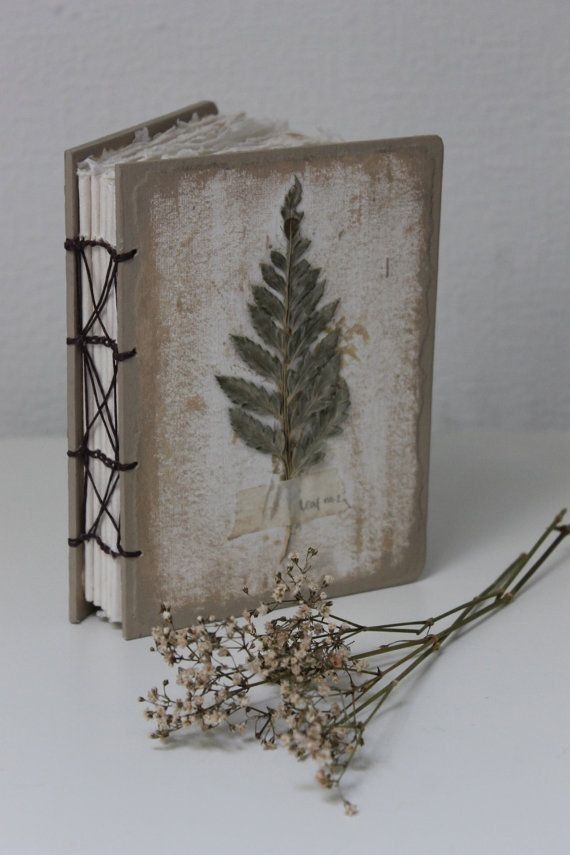 an old book with a plant on it next to some dried flowers and string wrapped around the pages