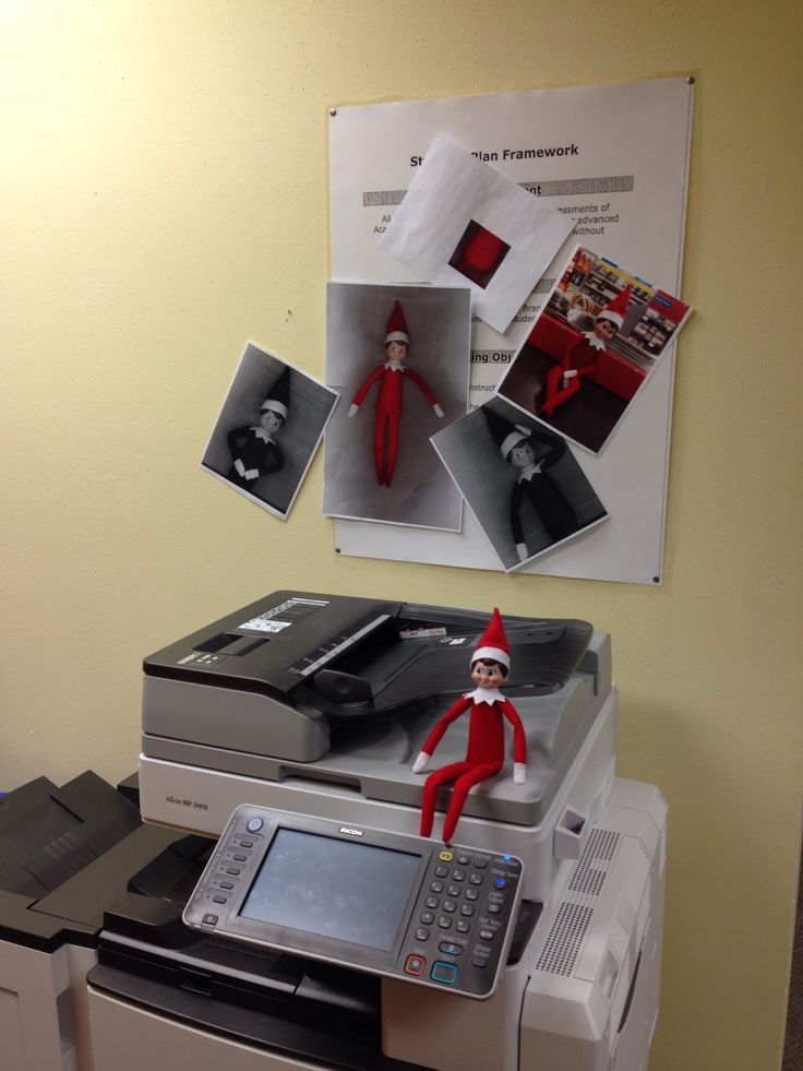 an elf is sitting on top of a printer in front of a poster with photos