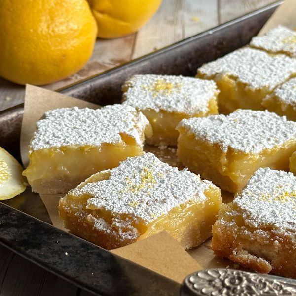 lemon bars with powdered sugar on top sit in a pan next to sliced lemons