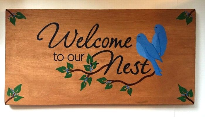 a wooden sign that says welcome to our nest with a blue bird perched on the branch