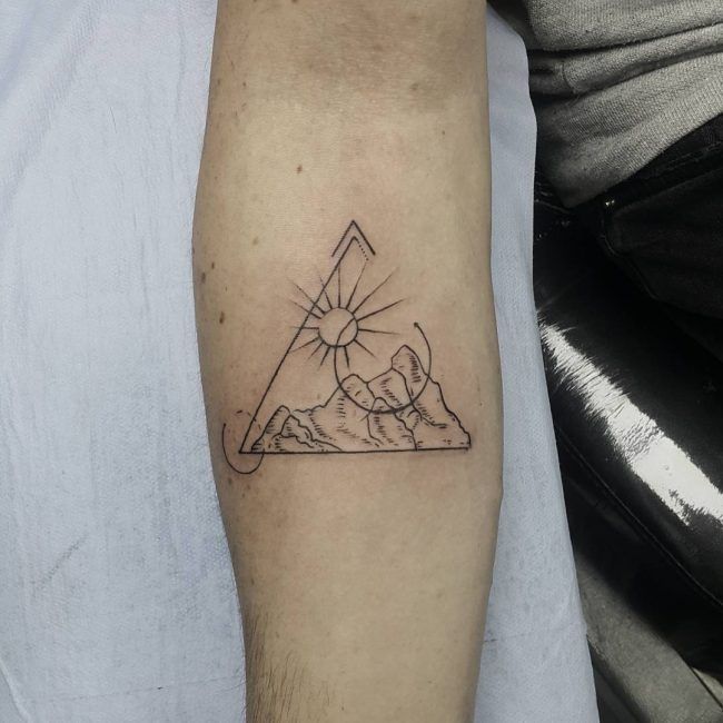 a man's arm with a tattoo on it that has a triangle and mountains in the background