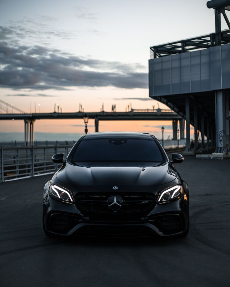 a black car parked in front of a building near the ocean at sunset or dawn