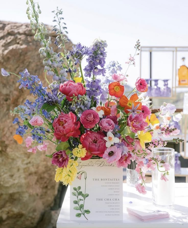 a vase filled with lots of colorful flowers on top of a white table next to a rock