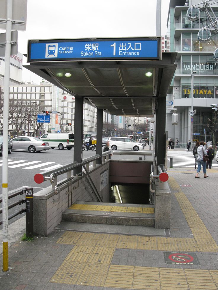 an entrance to a subway station with people walking around it and cars parked in the background