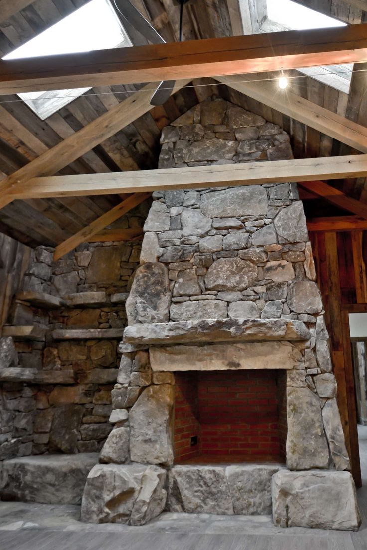 an old stone fireplace in the middle of a room with wooden beams and wood flooring