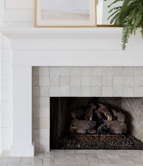 a white fireplace with a painting on the wall and a potted plant above it