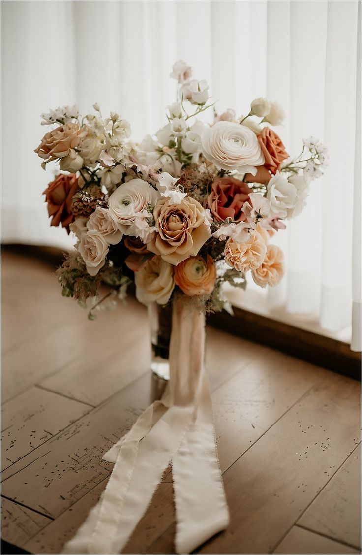 a bridal bouquet is sitting on the floor in front of a window with sheer curtains