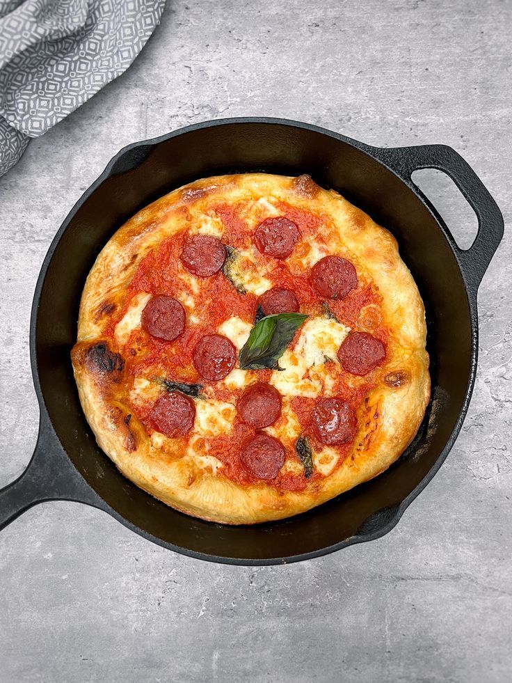 a pepperoni and cheese pizza in a cast iron skillet on a gray surface